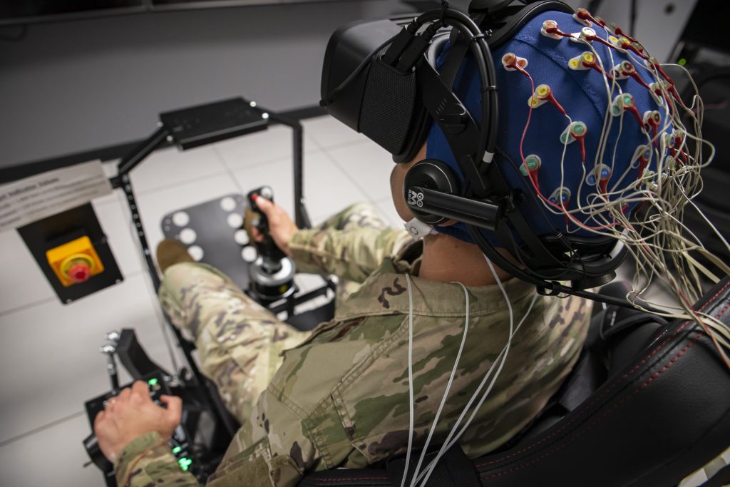 An Air Force Master Sergeant performs an exercise with virtual reality goggles and wires connected to his head.