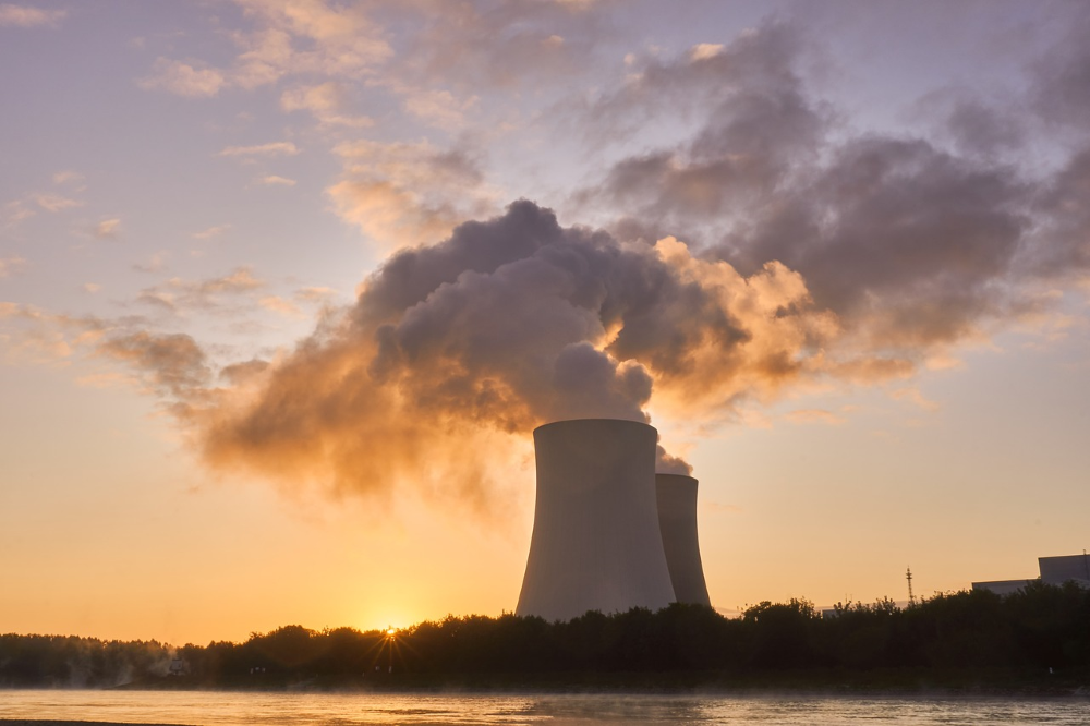 Nuclear Tower Stacks along river bank emits vapor clouds. Sun sets behind tower stacks.