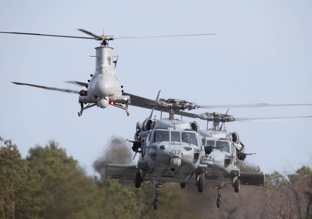 Two helicopters follow behind an unmanned aircraft.