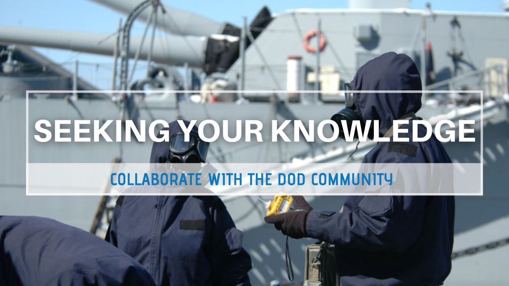 Military personnel wearing radiological protection gear talk next to a naval vessel.