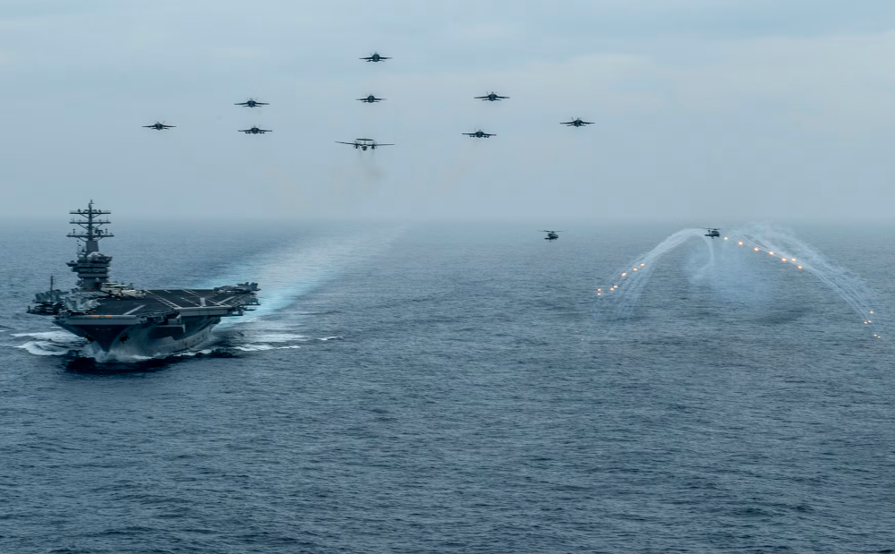 One naval vessel and eleven aircraft traveling over a body of water.