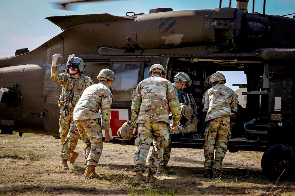 Five servicemembers preparing an injured servicemember for transport in a helicopter in a military exercise.