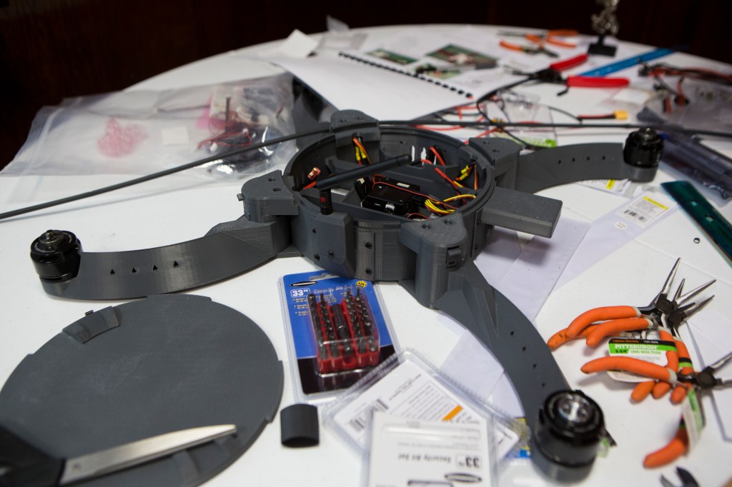 A partially completed drone. The cover on the body is open revealing wiring, and the rotor blades are not yet attached.