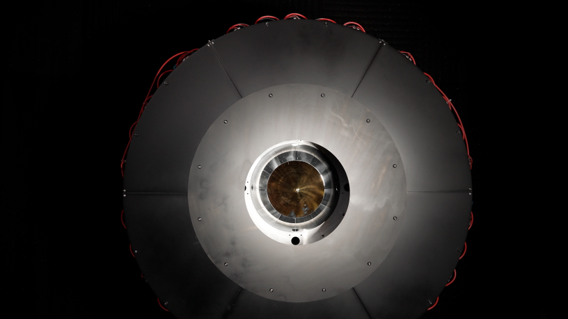 In the optical power beaming receiver designed for PRAD, the laser enters the center aperture, strikes a parabolic mirror, and reflects onto dozens of photovoltaic cells arranged around the inside of the device which convert the energy back to usable power. Source: DARPA