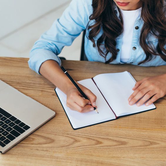 partial view of woman making notes while taking part in webinar in office