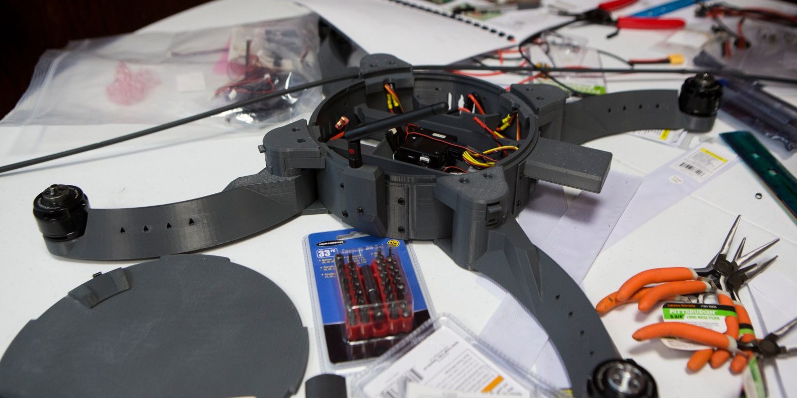 A partially completed drone. The cover on the body is open revealing wiring, and the rotor blades are not yet attached.