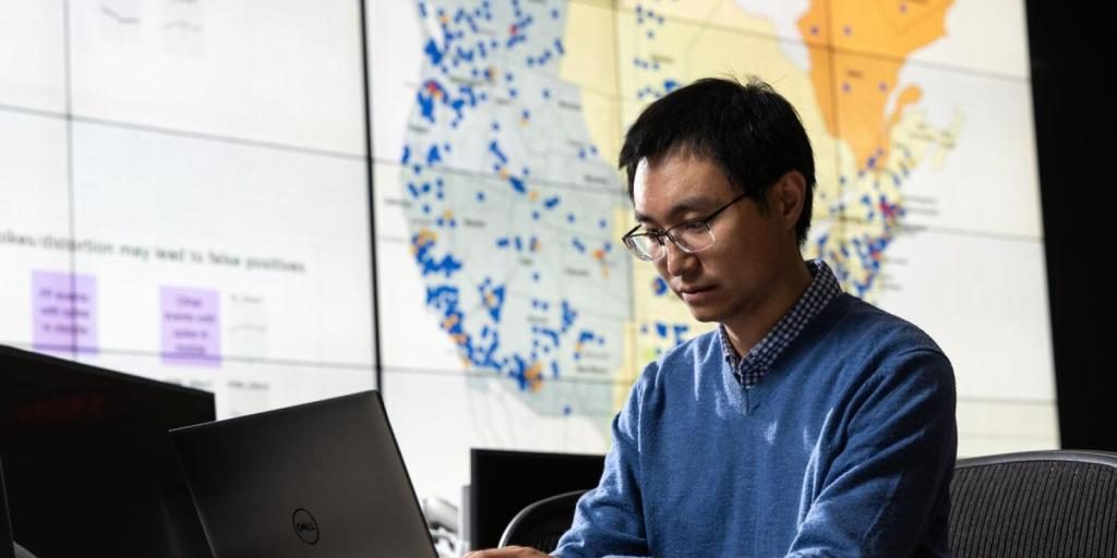 A man looks at the computer monitor with a map in the background