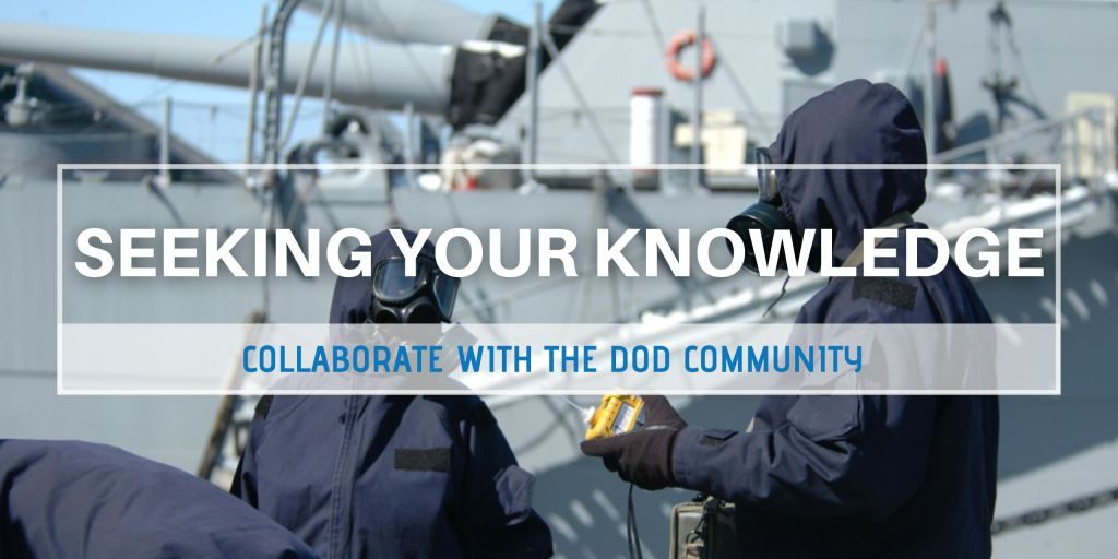 Military personnel wearing radiological protection gear talk next to a naval vessel.