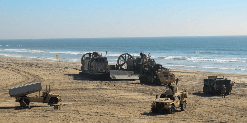 Several military vehicles staged on a beach for an All-Service logistics exercise.