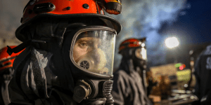 A U.S. Army reserve soldier participates in a CBRN exercise, wearing a gas mask and orange helmet.