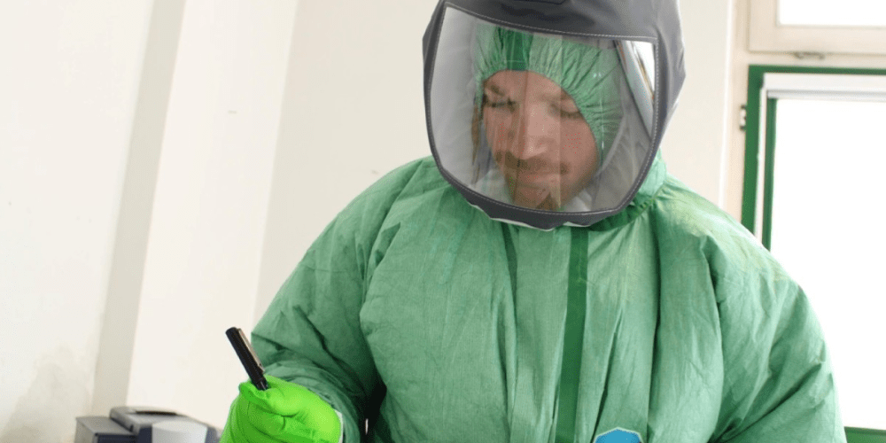 Department of Defense personnel in protective equipment writing on paper on a clipboard.