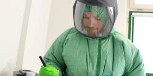 Department of Defense personnel in protective equipment writing on paper on a clipboard.