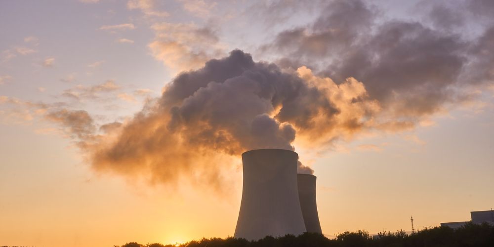 Nuclear Tower Stacks along river bank emits vapor clouds. Sun sets behind tower stacks.