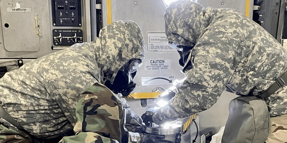 Military Personnel with protective equipment hold a container