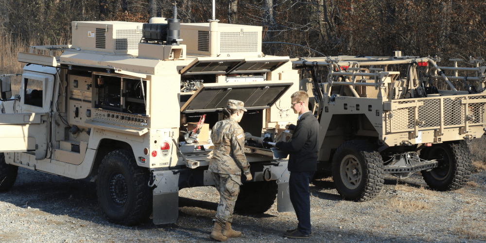 PNGoriginal Image of two people conversing behind a mobile military vehicle.