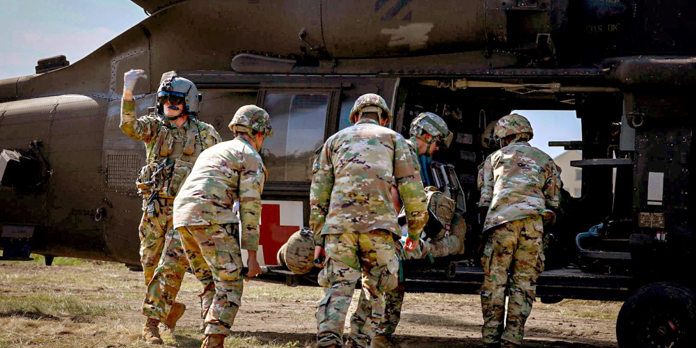 Five servicemembers preparing an injured servicemember for transport in a helicopter in a military exercise.