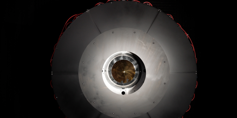 In the optical power beaming receiver designed for PRAD, the laser enters the center aperture, strikes a parabolic mirror, and reflects onto dozens of photovoltaic cells arranged around the inside of the device which convert the energy back to usable power. Source: DARPA