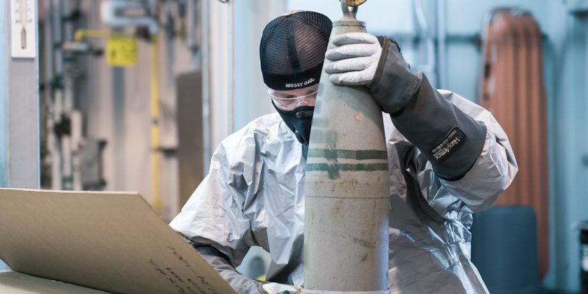 A munitions handler places a 155-mm projectile containing mustard agent into a box to begin the destruction process in the Static Detonation Chamber at the Blue Grass Chemical Agent-Destruction Pilot Plant. The last mustard-agent projectile was processed on September 4, and the mustard destruction campaign is complete. (A portion of this photograph has been blurred in accordance with Department of Defense guidelines.)